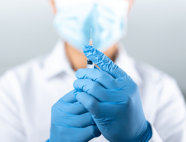 A gloved health care professional preparing a syringe